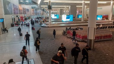 Toronto, ON, Kanada - 1 Mayıs 2025: Toronto Pearson Uluslararası Havalimanı 'ndaki insan, bagaj vagonu ve varış bilgileri sergilenen bir terminalin içini gösteren yüksek bir manzara.