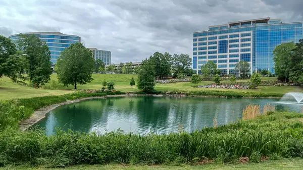 Charlotte, NC, ABD - 30 Nisan 2025: Modern ofis binaları yeşil çimenlerin, ağaçların ve Ballantyne Corporate Park 'ta bulutlu bir gökyüzünün altında bir yürüyüş yolunun ortasında duruyor.