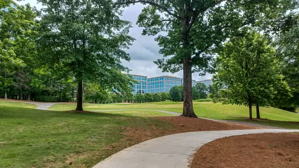Charlotte, NC, ABD - 30 Nisan 2025: Modern ofis binaları yeşil çimenlerin, ağaçların ve Ballantyne Corporate Park 'ta bulutlu bir gökyüzünün altında bir yürüyüş yolunun ortasında duruyor.