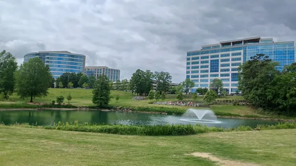 Charlotte, NC, ABD - 30 Nisan 2025: Modern ofis binaları yeşil çimenlerin, ağaçların ve Ballantyne Corporate Park 'ta bulutlu bir gökyüzünün altında bir yürüyüş yolunun ortasında duruyor.