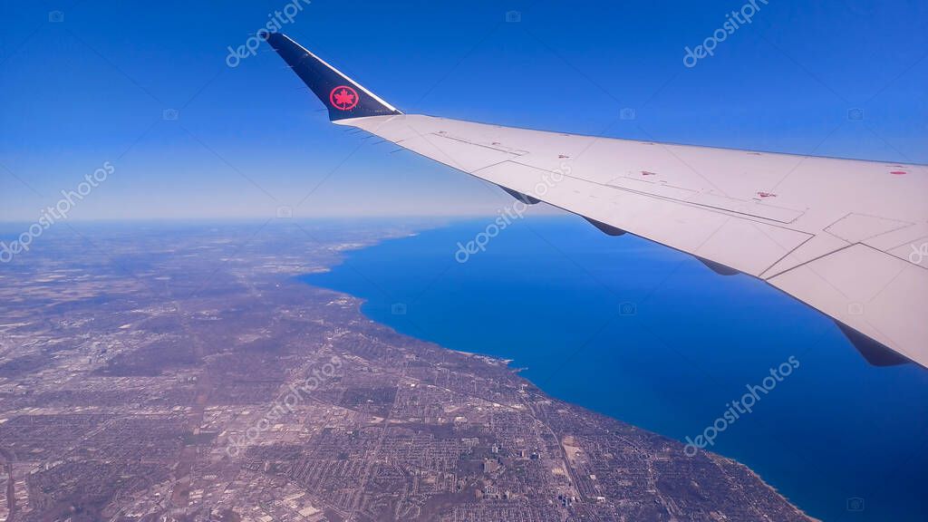 Toronto, ON, Canada - May 1, 2025: The wing and tail fin with the Air Canada maple leaf logo are visible above a layer of clouds during a flight.