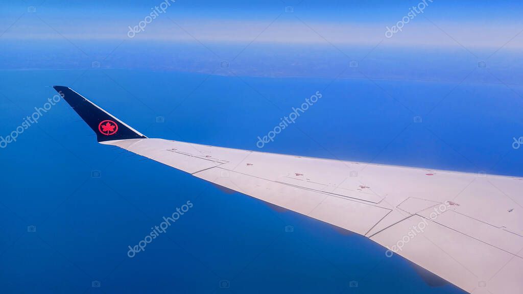 Toronto, ON, Canada - May 1, 2025: The wing and tail fin with the Air Canada maple leaf logo are visible above a layer of clouds during a flight.