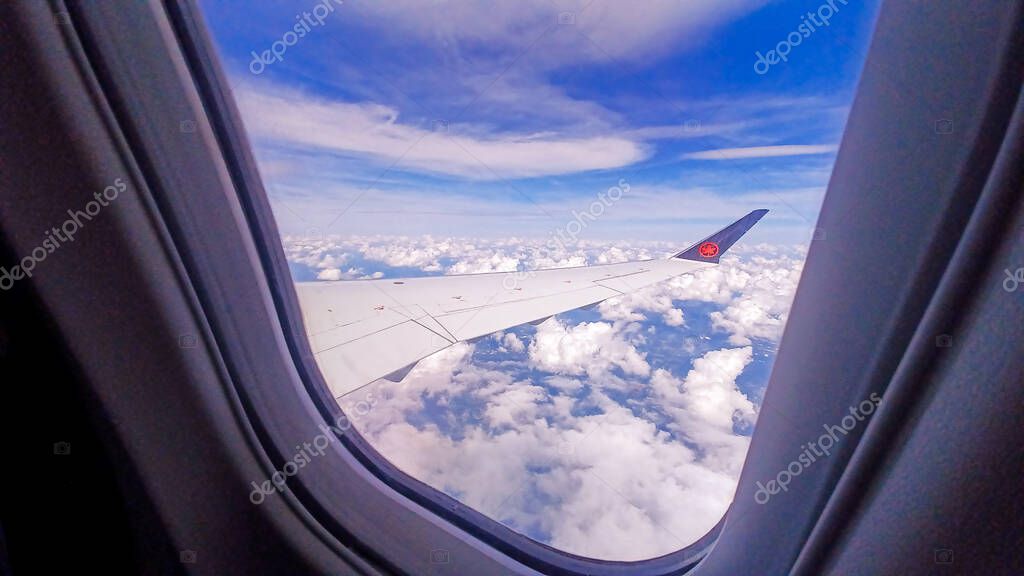 Toronto, ON, Canada - May 1, 2025: The wing and tail fin with the Air Canada maple leaf logo are visible above a layer of clouds during a flight.