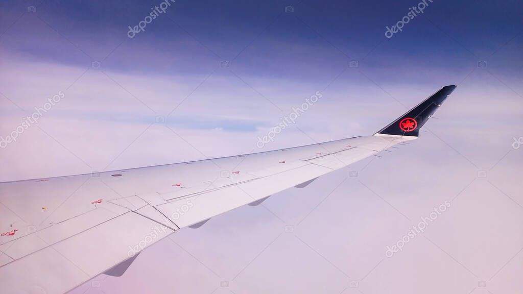 Toronto, ON, Canada - May 1, 2025: The wing and tail fin with the Air Canada maple leaf logo are visible above a layer of clouds during a flight.