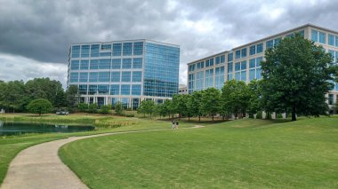 Charlotte, NC, ABD - 30 Nisan 2025: Modern ofis binaları yeşil çimenlerin, ağaçların ve Ballantyne Corporate Park 'ta bulutlu bir gökyüzünün altında bir yürüyüş yolunun ortasında duruyor.