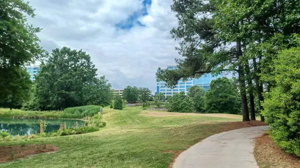 Charlotte, NC, ABD - 30 Nisan 2025: Modern ofis binaları yeşil çimenlerin, ağaçların ve Ballantyne Corporate Park 'ta bulutlu bir gökyüzünün altında bir yürüyüş yolunun ortasında duruyor.
