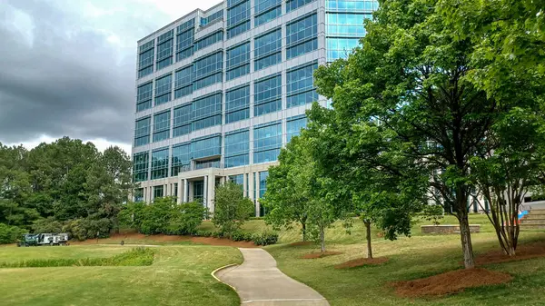 Charlotte, NC, ABD - 30 Nisan 2025: Modern ofis binaları yeşil çimenlerin, ağaçların ve Ballantyne Corporate Park 'ta bulutlu bir gökyüzünün altında bir yürüyüş yolunun ortasında duruyor.