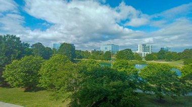 Charlotte, NC, ABD - 28 Nisan 2025: Berrak bir gökyüzü altında modern ofis ve yerleşim binalarıyla çevrili yemyeşil ağaçlar ve küçük bir gölet.