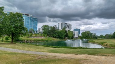 Charlotte, NC, ABD - 30 Nisan 2025: Modern ofis binaları yeşil çimenlerin, ağaçların ve Ballantyne Corporate Park 'ta bulutlu bir gökyüzünün altında bir yürüyüş yolunun ortasında duruyor.