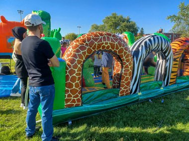 Toronto, ON, Kanada 31 Mayıs 2024: Aileler güneşli bir öğleden sonra bir çocuk etkinliğinde büyük şişme slaytlar ve engelli parkurların etrafında toplandılar..