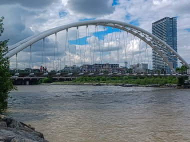Toronto, ON, Kanada 11 Temmuz 2024: İkonik Humber Körfezi Kemer Köprüsü arkaplanda yüksek binalar bulunan arkaplanda parçalı bulutlu bir gökyüzü altında nehir boyunca uzanır..