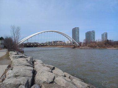 Toronto, ON, Kanada 11 Temmuz 2024: İkonik Humber Körfezi Kemer Köprüsü arkaplanda yüksek binalar bulunan arkaplanda parçalı bulutlu bir gökyüzü altında nehir boyunca uzanır..