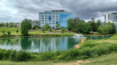 Charlotte, NC, ABD - 30 Nisan 2025: Modern ofis binaları yeşil çimenlerin, ağaçların ve Ballantyne Corporate Park 'ta bulutlu bir gökyüzünün altında bir yürüyüş yolunun ortasında duruyor.