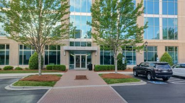 Charlotte, NC, ABD 29 Nisan 2025: Modern bir ofis girişinde ağaçlar ve peyzajlar yer almaktadır. Park halindeki arabalar görünür...