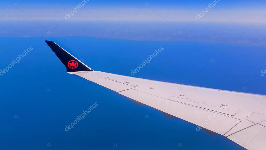 Toronto, ON, Canada - May 1, 2025: The wing and tail fin with the Air Canada maple leaf logo are visible above a layer of clouds during a flight.