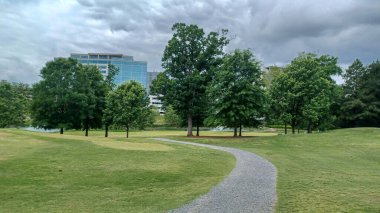 Charlotte, NC, ABD - 30 Nisan 2025: Modern ofis binaları yeşil çimenlerin, ağaçların ve Ballantyne Corporate Park 'ta bulutlu bir gökyüzünün altında bir yürüyüş yolunun ortasında duruyor.