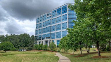 Charlotte, NC, ABD - 30 Nisan 2025: Modern ofis binaları yeşil çimenlerin, ağaçların ve Ballantyne Corporate Park 'ta bulutlu bir gökyüzünün altında bir yürüyüş yolunun ortasında duruyor.