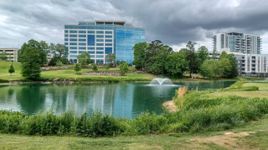 Charlotte, NC, ABD - 30 Nisan 2025: Modern ofis binaları yeşil çimenlerin, ağaçların ve Ballantyne Corporate Park 'ta bulutlu bir gökyüzünün altında bir yürüyüş yolunun ortasında duruyor.