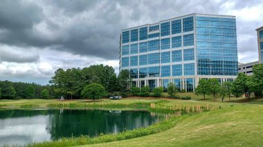 Charlotte, NC, ABD - 30 Nisan 2025: Modern ofis binaları yeşil çimenlerin, ağaçların ve Ballantyne Corporate Park 'ta bulutlu bir gökyüzünün altında bir yürüyüş yolunun ortasında duruyor.