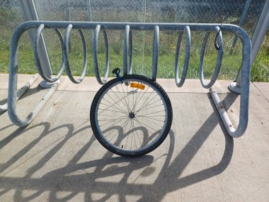 Toronto, ON, Kanada - 5 Ekim 2025: Terk edilmiş bir bisiklet tekerleği güneşli bir günde beton bir kaldırımda metal spiral bisiklet parkına kilitli kalır.