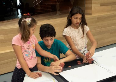 Üç çocuk bir odada masa oyunlarıyla oynuyorlar, takım olarak oynuyorlar, birlikte inşa ediyorlar, birbirlerine yardım ediyorlar.