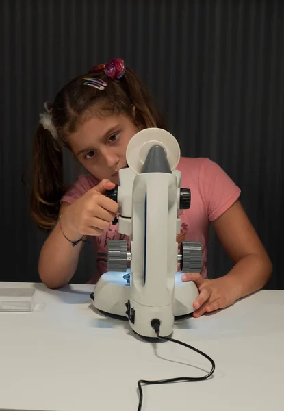 8-9 year old girl adjusts the viewfinder of a microscope to be able to look through it. science classes