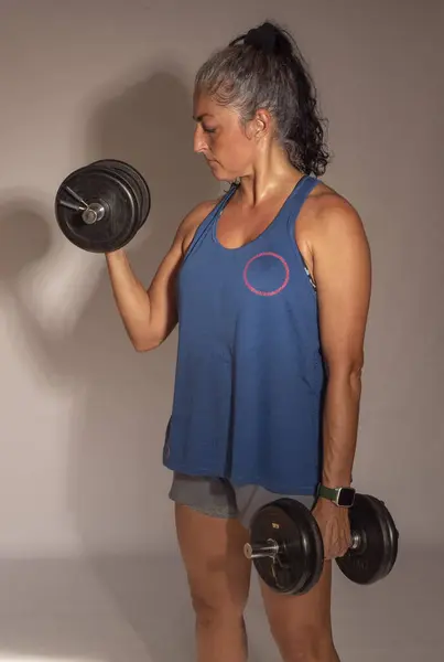 adult woman wearing sports clothes, holding dumbbells, doing sports, building up her biceps, strength training for 45 year old women, best version, healthy living
