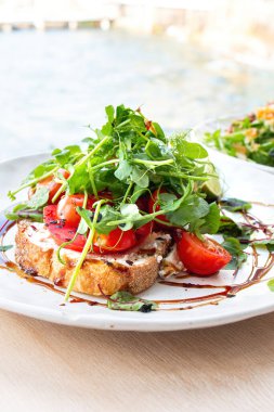 Lezzetli domatesler tost dilimlerinde ve bezelye filizleri ahşap masada süslenmiş taze yeşil lahanalar gün ışığında kumsalda manzaralı bir kafede arka planda..