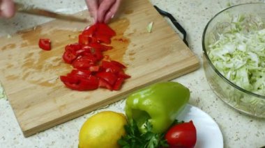 Sebze salatası pişirmek için sebzeli parlak mutfak masası. Yakın plan kadınlar domatesleri kesip salata kasesine koyar. Sağlıklı gıda konsepti. Çiğ gıda, vejetaryenlik ve vejetaryenlik.