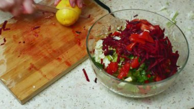 Bir kadın elinin limonu kestiği ve onu taze sebze salatasıyla bir kaseye sıkıştırdığı yakın plan. Sebze salatalı parlak mutfak masası. Sağlıklı vejetaryen ve vejetaryen yaşam tarzı.