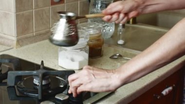 Ev mutfağında bir kadın Türk kahve makinesinde sabah kahvesini hazırlıyor. Ev hanımı parlak mutfak masasından çakmağı alır, gaz sobasını yakar, ateşe cemve koyar ve kahveyi çay kaşığıyla karıştırır..