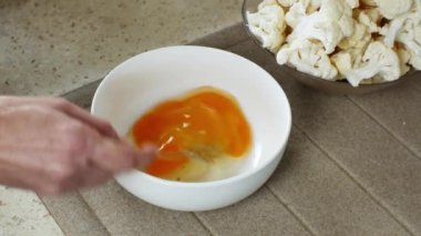 Yakın plan dişi elleri, arka planda karnabahar parçalarıyla beyaz cam bir kasede demir çatalla yumurtaları karıştırır. Ev yemeği kavramı: Doğal, sağlıklı ve sağlıklı yiyecekler..