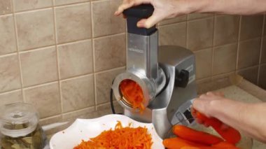 Yemek işlemcisine kırmızı havuç süren kadın ellerinin yakın çekimi. Olgun taze sebzeleri işliyorum. Ev mutfağında ev aletleri kavramı.