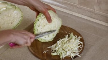 Mutfak masasındaki tahta kesme tahtasının üzerinde beyaz lahana doğrayan kadın elleri. Taze çiğ sebze kesiyorum. Sağlıklı vejetaryenlik ve vejetaryen beslenme kavramı.