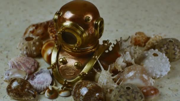 老式铜制潜水头盔 有一个孔 背景上有许多不同的漂亮的海贝壳 平面躺在一个海洋主题上 — 图库视频影像