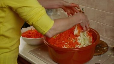 Bir ev hanımı büyük bir kasede rendelenmiş kırmızı havuçla doğranmış beyaz lahanayı karıştırıyor. Kış için taze sebze topluyorum. Konserve sebzeleri uzun süre saklamak kolaydır..