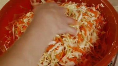 Yakın plan kadın elleri mutfak masasındaki büyük kasede parçalanmış beyaz lahana ve kırmızı havuçları karıştırır. Kış için taze sebzeleri tuzluyorum. Sebze reçelleri.