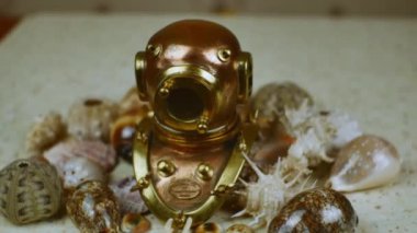 Pek çok farklı güzel deniz kabuğunun arka planında lombozlu klasik bakır dalış kaskı. Bir deniz temasının üzerinde yatıyordu..