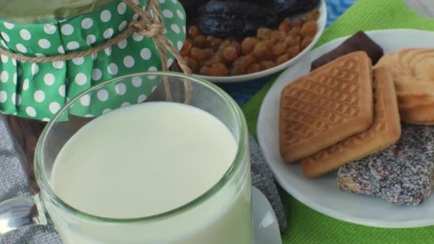 透明なガラスカップにミルク テーブルの上に小さじ1杯のジャムの瓶と ドライフルーツ レーズンとプルーン ソーサー上のお菓子やクッキー 甘い朝食のコンセプト — ストック動画