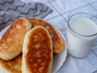 Masada, gri masa örtüsüyle kaplı, bir bardak taze süt ve lanet olası ev yapımı turtalarla dolu bir tabak var..