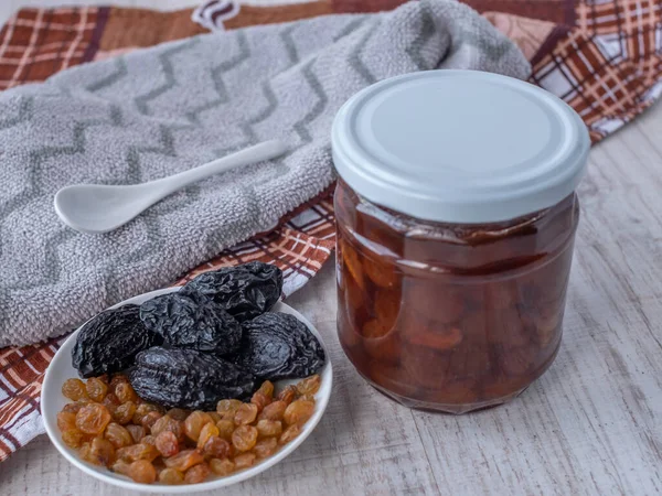 Bir kavanoz beyaz kiraz reçeli ve bir tabak kurutulmuş meyve, kuru üzüm ve kuru erik, beyaz cam bir çay kaşığı. Yukarıdan yakından yan görüntü. Sağlıklı ya da sağlıksız şeker seçimi kavramı