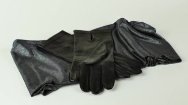 Yeşil ve altın sarısı bir eşarpta, açık arkaplanda izole edilmiş bir çift yeni siyah deri eldiven. Zarif kadınların siyah deri eldivenleri yeşil bir eşarbın üzerinde uzanmış, açık arkaplanda altın bir parıltı var..
