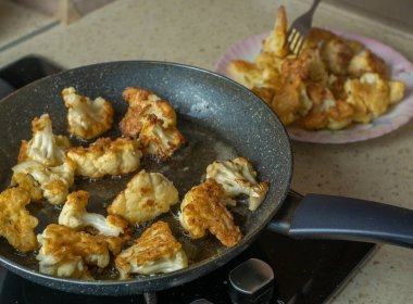 Kızarmış karnabahar parçalarını tavadan tabağa döken bir çatalla kadın elinin yakın çekimi. Bir ev hanımı kızarmış karnabahar parçalarını tavadan tabağa koyar..