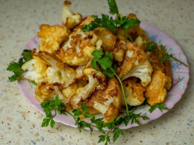 Beyaz bir tabakta hamurda pişmiş karnabahar tomurcukları, üzerine taze bitkiler serpilmiş. Odaklanma zorlanıyor, yakın plan. Seçici odaklanma. Sağlıklı sebze yemekleri pişirme kavramı