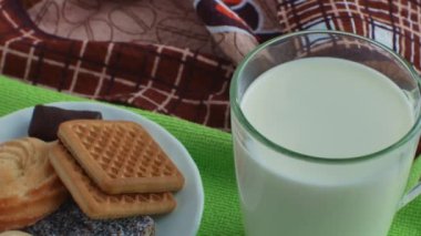 Yeşil bir peçeteye bir bardak taze süt ve bir tabak kurabiye ve şeker. Bisküviler ve şekerlemelerle dolu tatlı bir sütlü kahvaltıya yakın çekim. Çok fazla tatlı yemek sağlığın için kötüdür..