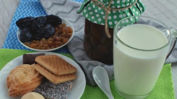 着色されたナプキンのテーブルの上に 牛乳のガラス ジャムの瓶 小さじ1杯 レーズン プルーン クッキー お菓子の2つのソーサー 朝食用製品のコンセプト — ストック動画