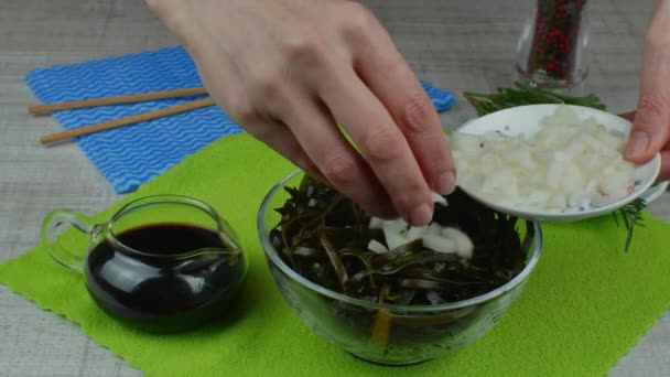 一位家庭主妇准备海藻沙拉 在一个透明的碗里 女性的小手将洋葱褐色的海藻撒入其中 烹调健康 健康的素食 健康生活方式的概念 — 图库视频影像