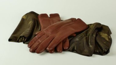 Yeşil ve altın sarısı bir eşarpta, açık arkaplanda izole edilmiş bir çift yeni kahverengi deri eldiven. Zarif kadınların kahverengi deri eldivenleri yeşil bir eşarbın üzerinde uzanmış açık arkaplanda altın bir parıltı.