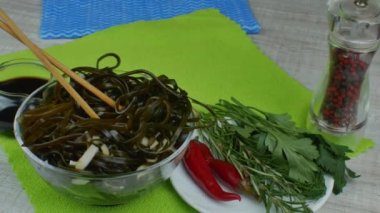 Seramik kasede yosun salatası ve ahşap yemek çubukları. Lezzetli yosun salatasıyla dönen kase, çeşitli otlarla dolu bir tabak ve kırmızı biber, soya soslu sos kasesi. Deniz ürünleri yemeği kavramı.