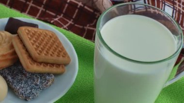 A glass of milk and a plate with sweets and cookies on a green napkin close-up. Sweet dessert. The concept of the dangers of sugar for health.